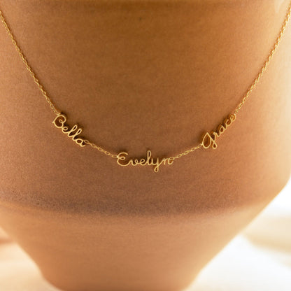 Gold tiny multiple name necklace with layered chain design, featuring personalized name charms on a delicate chain.